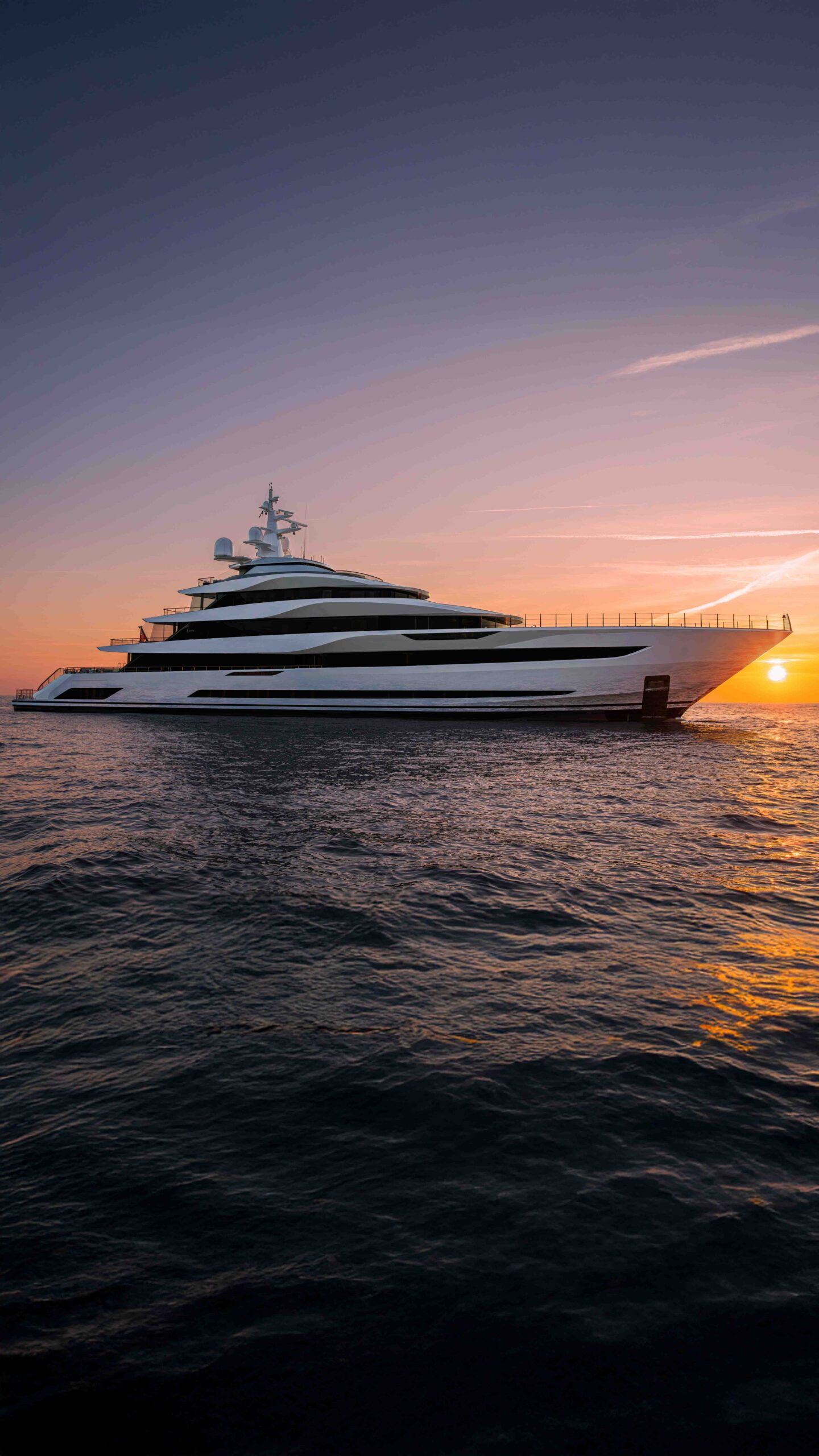 The superyacht Admiral Platinum sailing at sunset, with the golden light reflecting on the water.